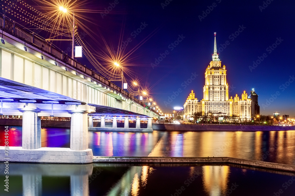 Stalin's skyscraper on the banks of the Moscow River in the illumination of evening lighting against the background of the sunset sky. Panorama
