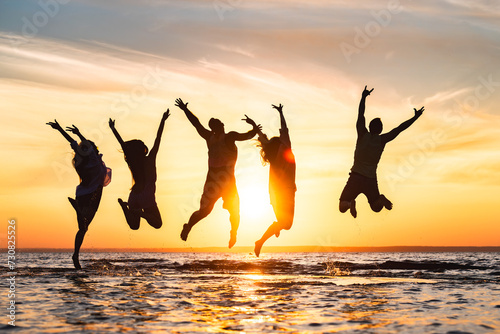Group of happy young friends are having fun and jumping at calm sunset beach