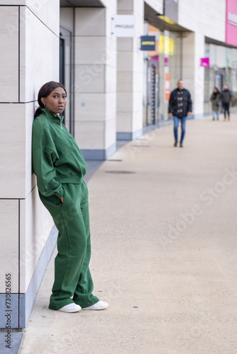 Foto This image captures a young African woman leaning against a building's exterior in an urban setting