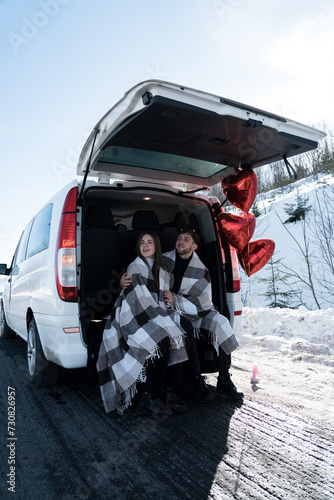 A couple in love is having a romantic date while traveling. A man and a woman are posing against the backdrop of snowy mountains, drinking tea. Travel concept