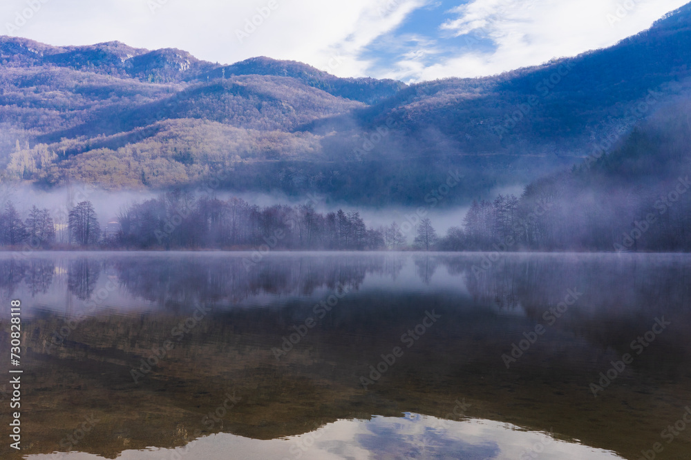 An impressive landscape with fog on the horizon and reflections of mountains, sky and forest on the lake