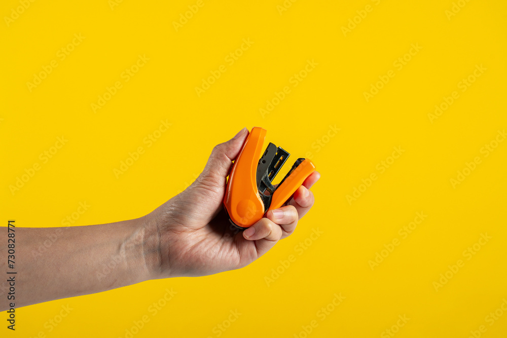 Orange stapler in hand isolated on yellow background
 - obrazy, fototapety, plakaty 