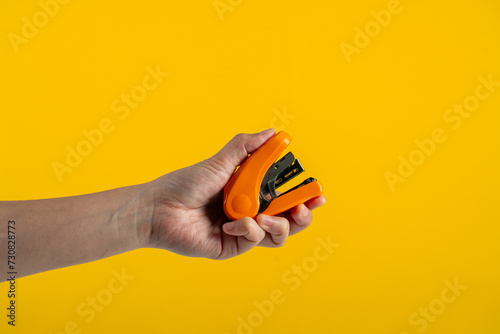 Orange stapler in hand isolated on yellow background
 photo
