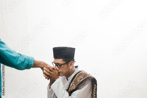 Asian Muslim man in white shirt with brown skin wearing koko shirt shaking hands with his parents on white studio background, traditional indonesian sungkem concept