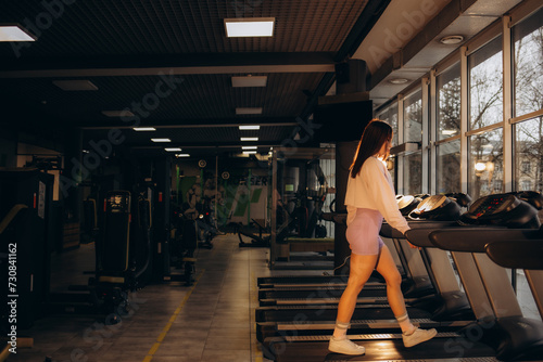 Woman running on treadmill at a panoramic window and listening to music via headphone at gym. Concept of healthy lifestyle.