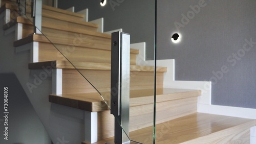 Interior design stylish wooden stairs inside the house with modern glass railings and walls decorated with trendy lamps
