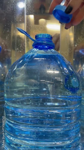 A woman draws drinking water from a purified water vending machine and screws the cap on a five-liter plastic bottle with her hand. The bottle is filled with drinking water. Vertical video.