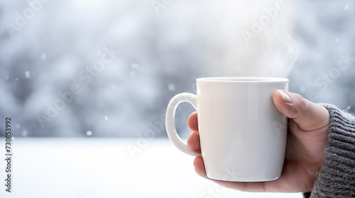 Close-up of a person holding a steaming mug against a snowy backdrop  snowflakes visible in the air