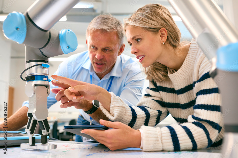 Male Tutor And Female College Or University Engineering Student In Robotics Class Studying Robot Arm Male Tutor And Female College Or University Engineering Student In Robotics Class Studying Robot Arm
