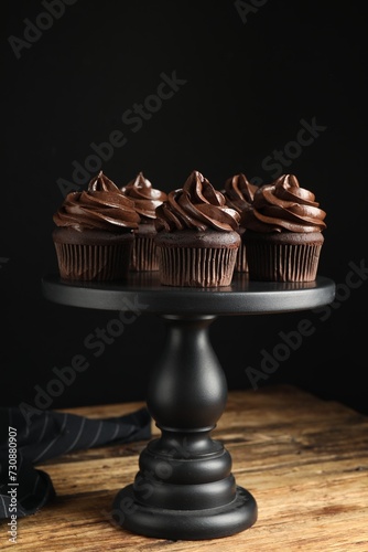 Dessert stand with delicious chocolate cupcakes on wooden table against black background