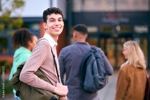 Portrait Of Male University Student Looking Over Shoulder With Friends Outside College Buildings