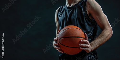 A focused athlete in a dark jersey holds a basketball against a dark background, emphasizing the readiness and determination for the game. 