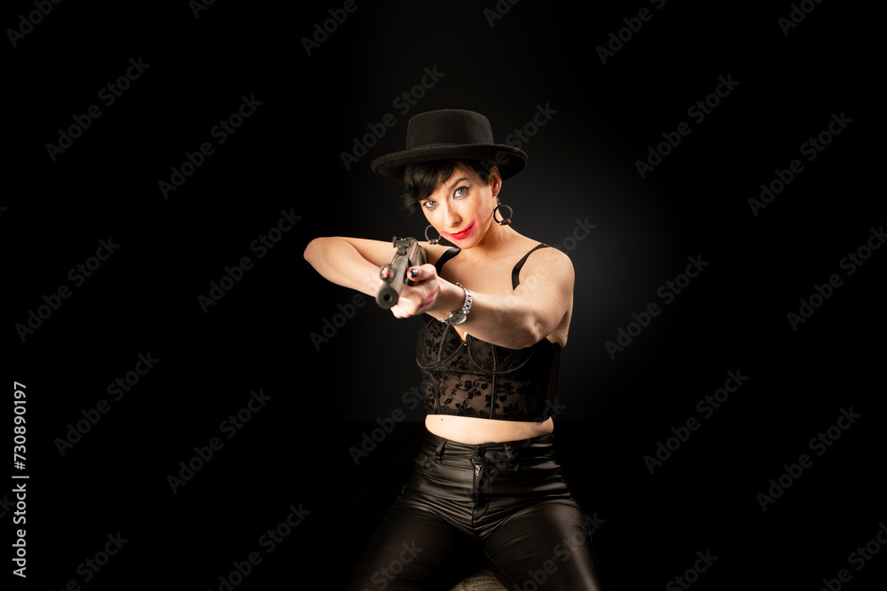 Young mentally unstable and paranoid woman with a gun in a black hat on a black background