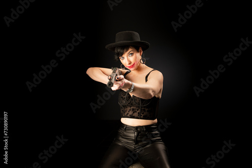 Young mentally unstable and paranoid woman with a gun in a black hat on a black background