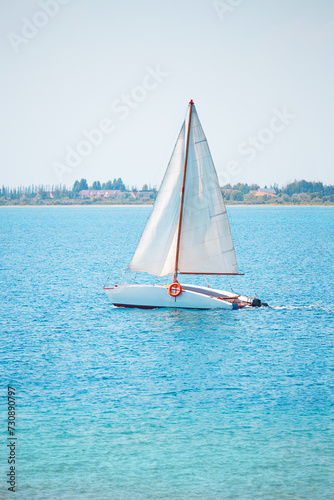 Sailing motor boat on the open sea in sunlight on the water. Behind are trees and houses on the shore. Leisure, sailing, regatta, adventure, relaxation