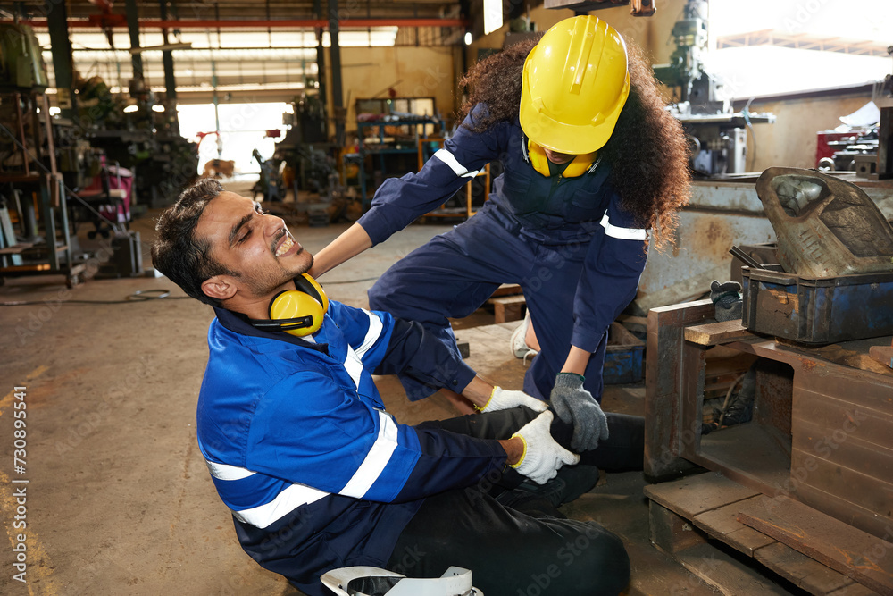 factory worker or engineer suffering from knee pain and coworker getting first aids help in the factory factory worker or engineer suffering from knee pain and coworker getting first aids help in the factory