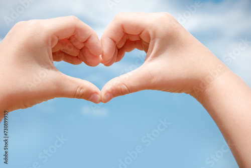 Two hands make a heart shape in the blue sky. © Julia