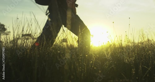 Man with dreadlocks and a backpack walking in a raised bog during foggy sunrise. Dew grass in foreground. Slow motion. photo