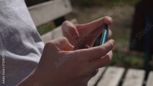 A child uses a turquoise smartphone on the street, pressing with a finger, plays, reads, communicates. Mobile phone in two hands.