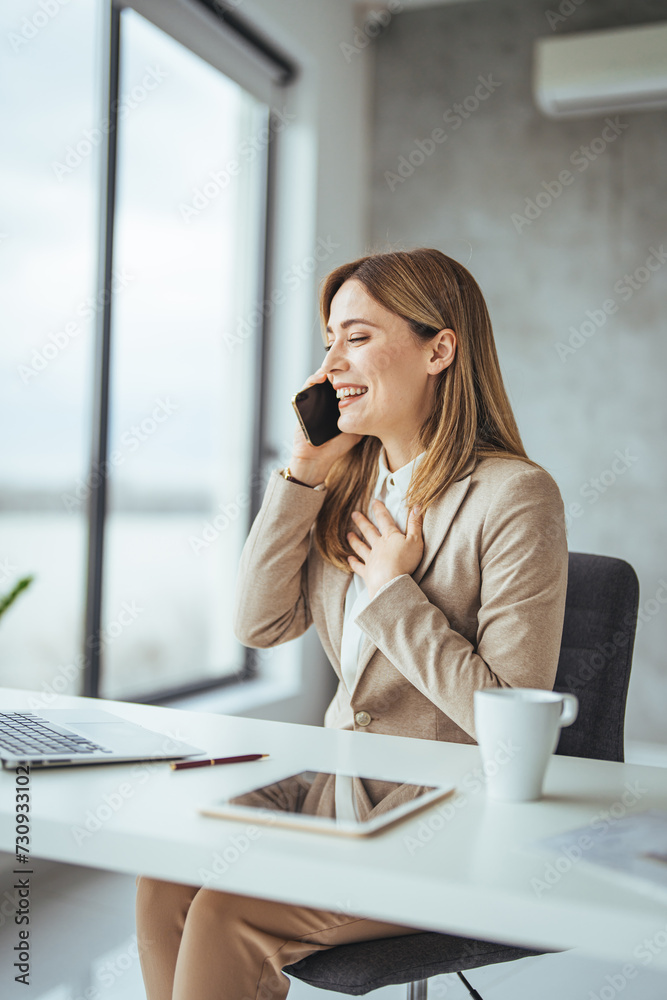 Happy freelancer using computer and talking on smart phone at office. Beautiful businesswoman working sitting at her desk in the office. Happy freelancer using computer and talking on smart phone at office. Beautiful businesswoman working sitting at her desk in the office.