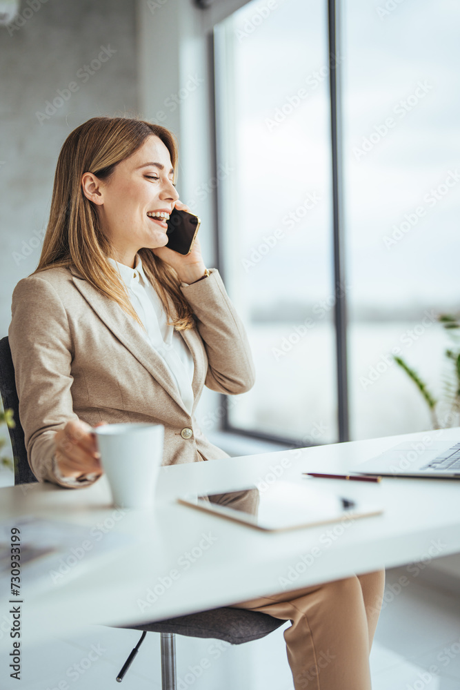 Happy freelancer using computer and talking on smart phone at office. Beautiful businesswoman working sitting at her desk in the office. 