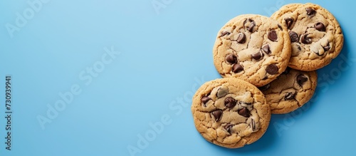 Four chocolate chip cookies are arranged in a stack on a blue background, creating a delicious and tempting finger food.