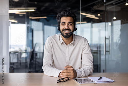 Portrait of a smiling Muslim man businessman, marketer, salesman sitting in the office at the table in a headset and smiling confidently at the camera photo