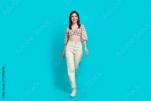 Full length photo of shiny pretty woman wear flower print top smiling walking isolated teal color background
