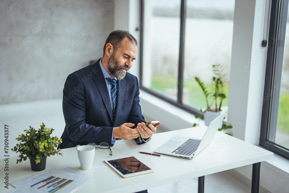 Mature business man in formal clothing wearing spectacles using mobile phone. Serious businessman using smartphone and digital tablet at work. Manager in suit using cellphone in a modern office. Mature business man in formal clothing wearing spectacles using mobile phone. Serious businessman using smartphone and digital tablet at work. Manager in suit using cellphone in a modern office.