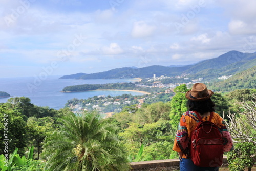 Woman tourists wears straw hat and carries a red backpack stand and look at the beauty of the Karon View point. in Phuket province of Thailand. The three bays are crescent shaped. It is popular place
