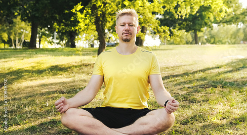 Young man sitting on a yoga mat in Lotus position with a closed eyes preparing to practice yoga outdoors. Fitness and healthy concept.
