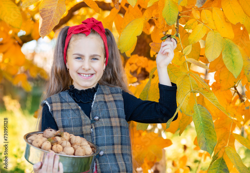 Smiling girl with red headband holds bowl of walnuts with autumn leaves in the background.