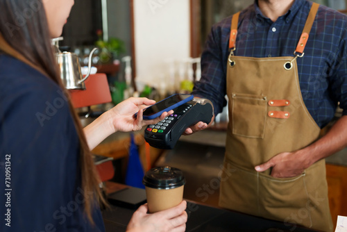 Male cafe employees various nationalities holding credit card acceptor QR code smiled. brunette female customer holding mobile phone scan payments holding disposable paper coffee cup small business. photo