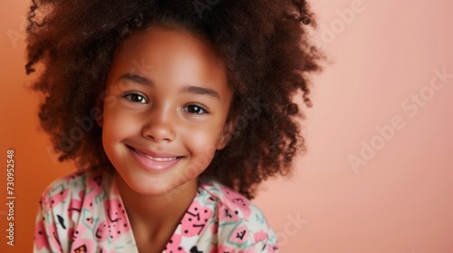 A young girl with a radiant smile showcasing her natural curly hair set against a warm soft-focus background. © iuricazac
