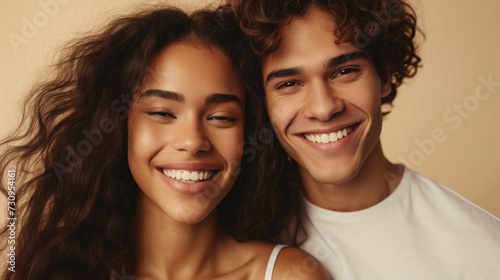 A close-up photograph of a smiling young woman with long curly hair and a young man with curly hair both appearing happy and enjoying each other's company.