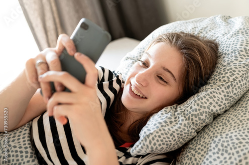 Teenage Girl Checking Social Medias And Messages On A Smartphone Lying On A Bed