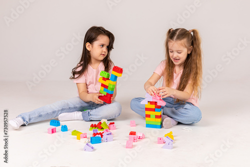 A happy kids girls collect a tower of colored cubes. The preschooler sits down at the white background and assembles the construction set. Girls smile, pleased with the result.