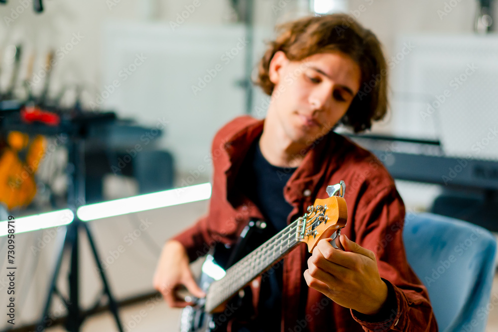 a musician with an electric guitar during a rehearsal in a recording studio adjusts the strings and the sound of the musical instrument