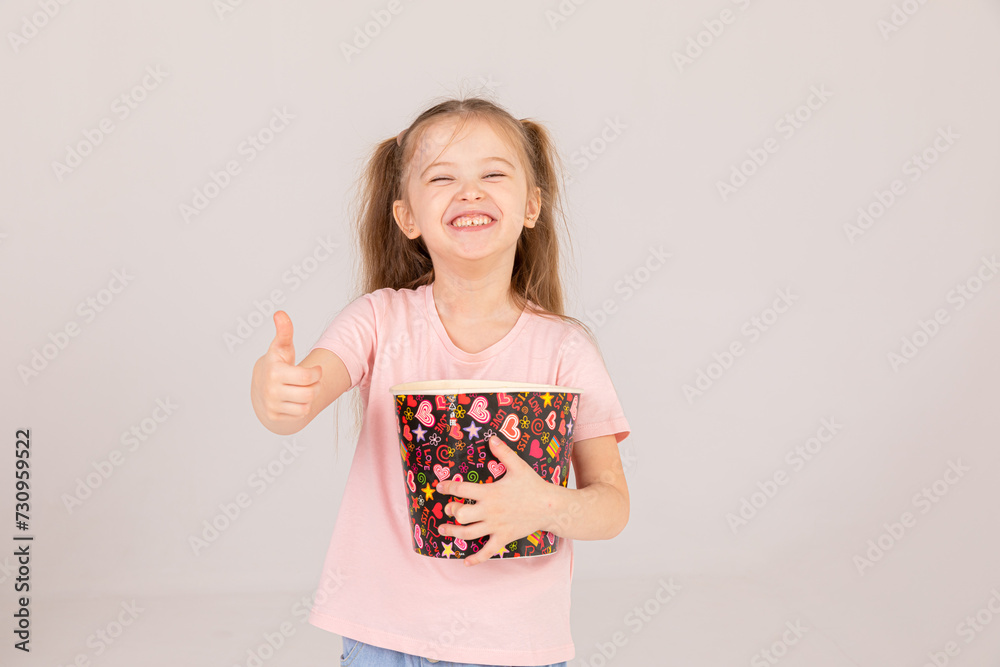 Cheerful little girl in 3D glasses watch the film while holding popcorn and show thumb up over white background. Cinema and movie concept Cheerful little girl in 3D glasses watch the film while holding popcorn and show thumb up over white background. Cinema and movie concept