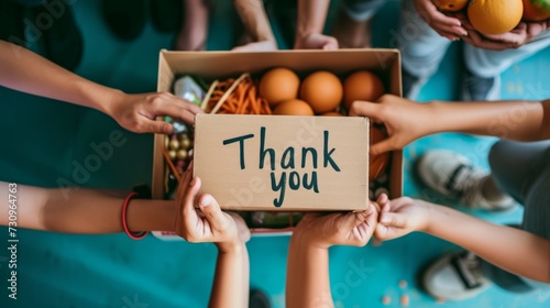 Volunteers expressing gratitude with a  thank you  message held over a box full of donated groceries photo