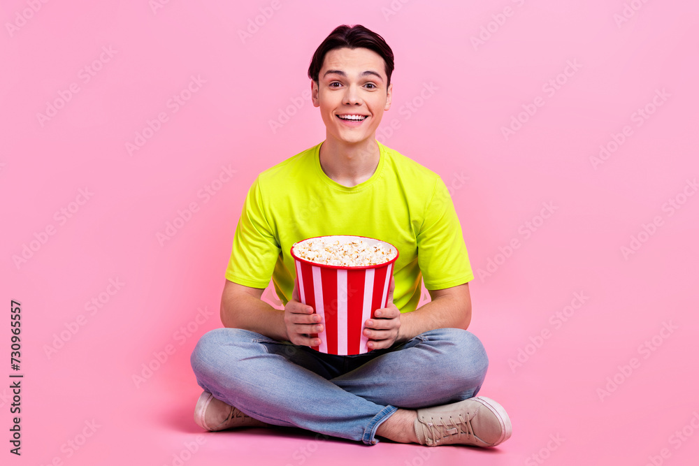 Full length photo of funny excited man dressed yellow t-shirt enjoying pop corn watching movie isolated pink color background Full length photo of funny excited man dressed yellow t-shirt enjoying pop corn watching movie isolated pink color background
