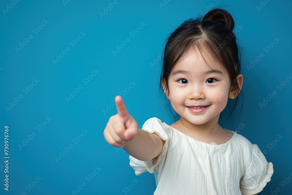 Asian child posing on blue background, pointing up Asian child posing on blue background, pointing up