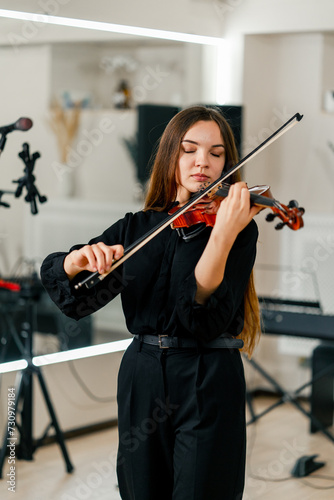 A young beautiful girl concentrates on performing a melody and enjoys playing the violin at a rehearsal in a music studio