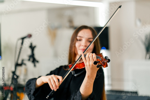 A young violinist plays with a bow on the strings of her violin against the background of musical instruments at the rehearsal base