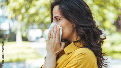 Portrait of unhealthy cute female in yellow top with napkin blowing nose, looks to the source of the allergy, place for advertising. Rhinitis, cold, allergy concept. Pollen allergy symptoms