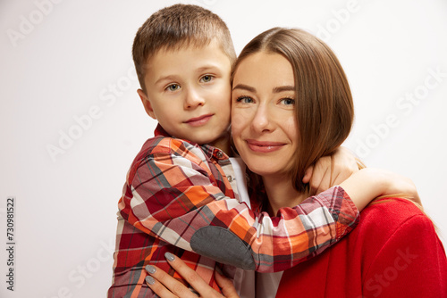 Portrait of beautiful, smiling young woman,mother posing with her little son, adorable boy against white studio background. Concept of happiness, Mother's day, childhood, fashion and lifestyle