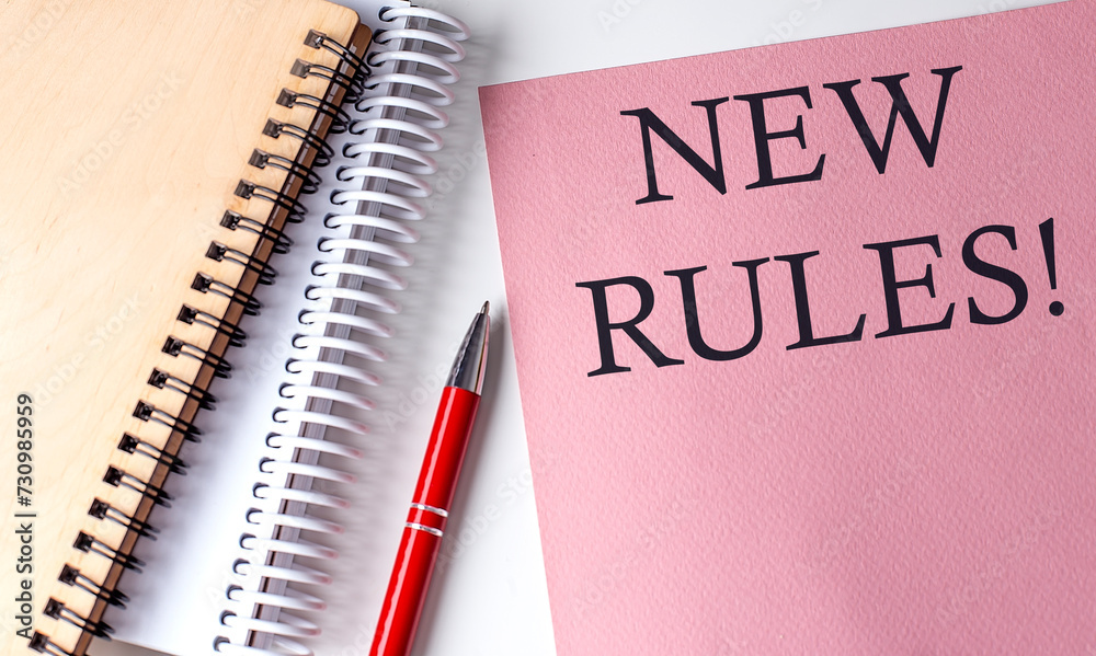 NEW RULES word on the pink paper with office tools on white background NEW RULES word on the pink paper with office tools on white background