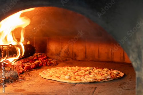 Baked tasty delicious pizza in a traditional oven with burning wood and shovel. 