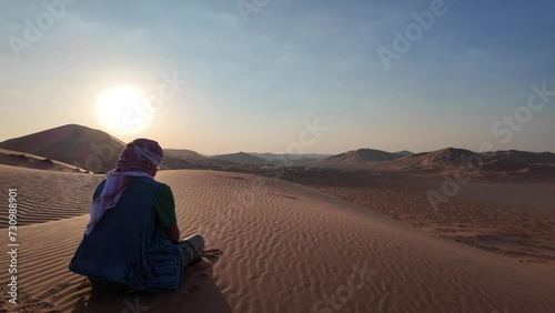 beduin man in vastness of the Empty Quarter with kefiah hat in contrast to the golden sand at dawn. He seeks adventure and solitude in land of Oman Rub' al-Khali desert. photo