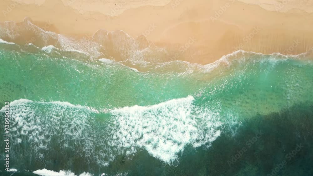 Aerial view of an empty sandy beach with slow moving beautiful waves on a sunny day.